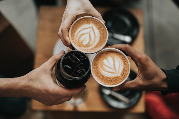 Three friends toasting with cappuccinos and an iced coffee